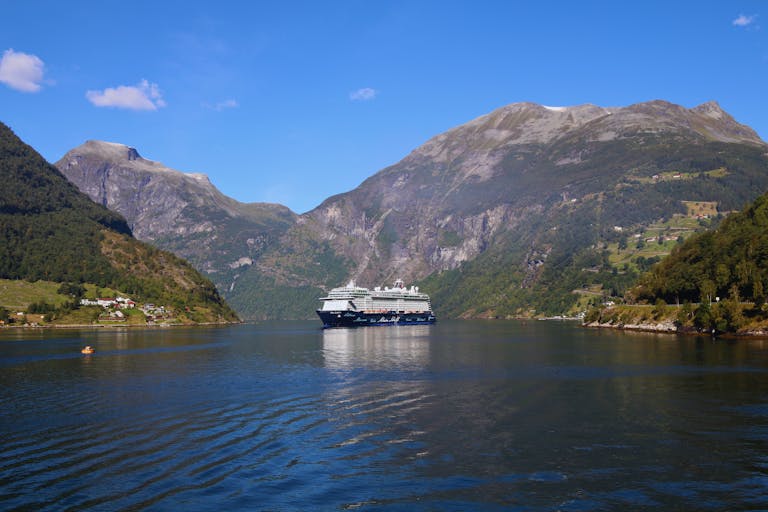 The Essential Cruise Shop Blog - A majestic cruise ship in the scenic Geiranger Fjord, surrounded by mountains.