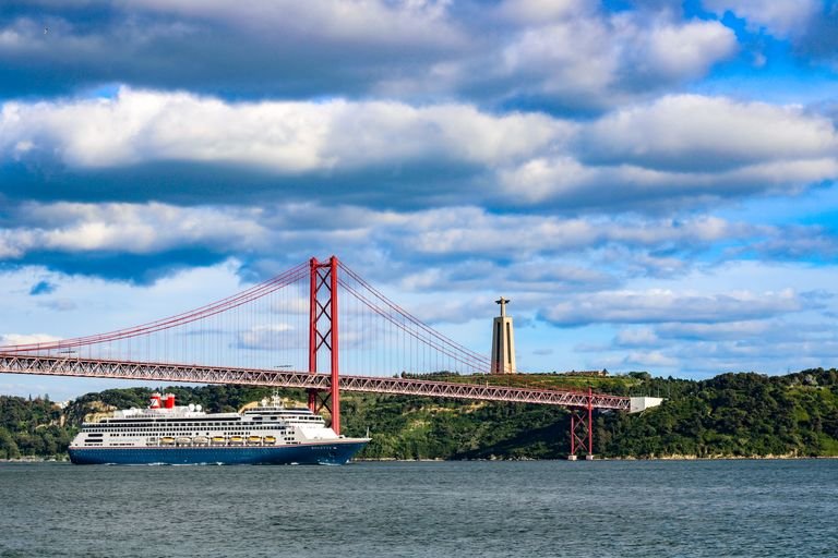 Scenic view of a Fred Olsen cruise ship sailing under the iconic 25 de Abril Bridge in Lisbon with Christ the King statue in background - The Essential Cruise Shop Blog
